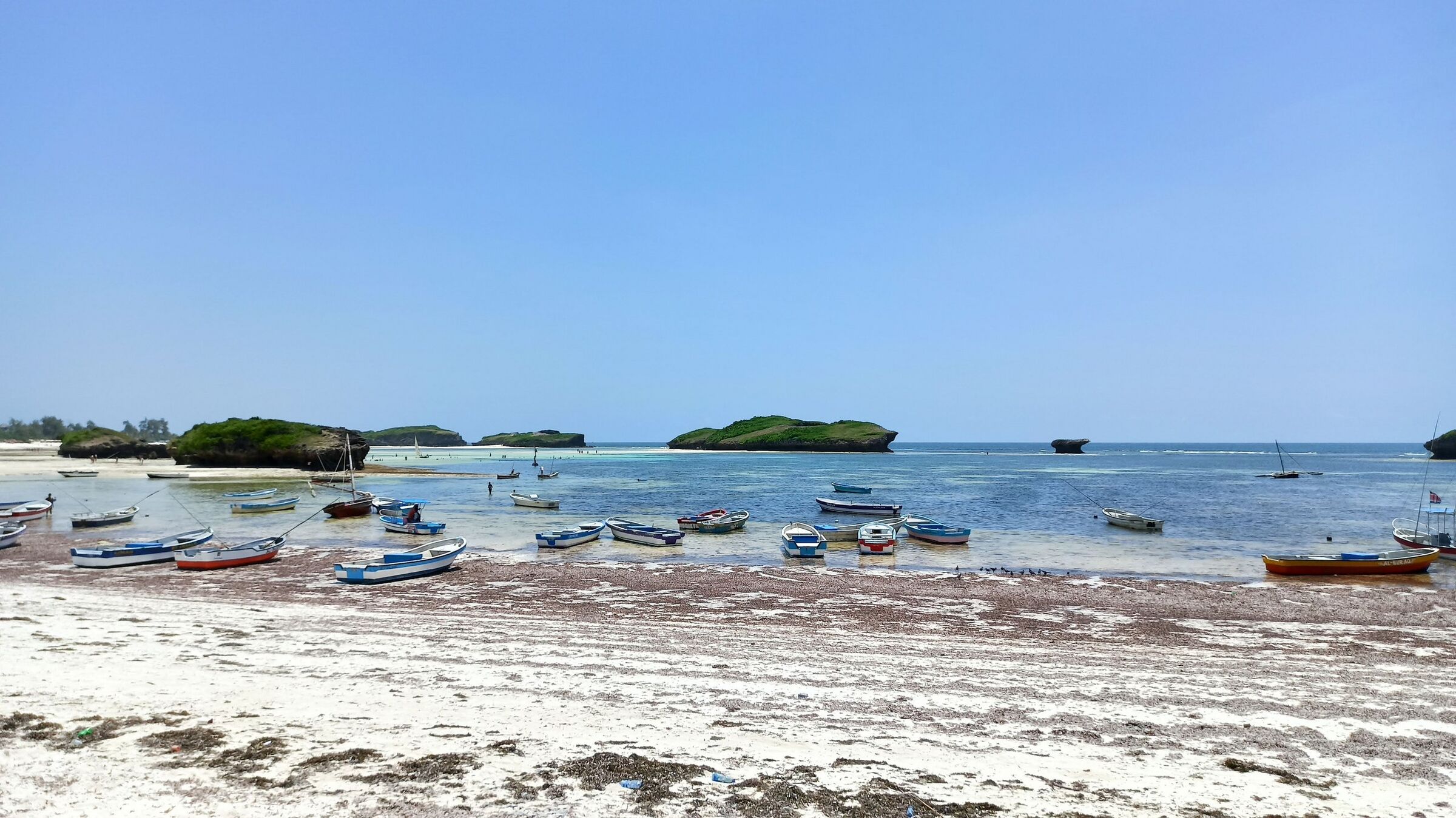 Small boats resting in the shallows at Watamu beach, with coral islets in the bay beyond.