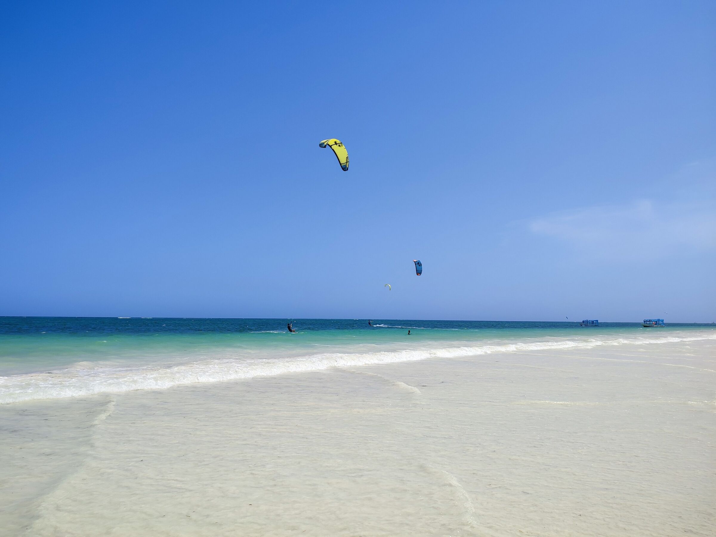 Kitesurfers with yellow and blue kites over turquoise water off a white sand beach at Diani during the Kenya Kite Cup in January 2022