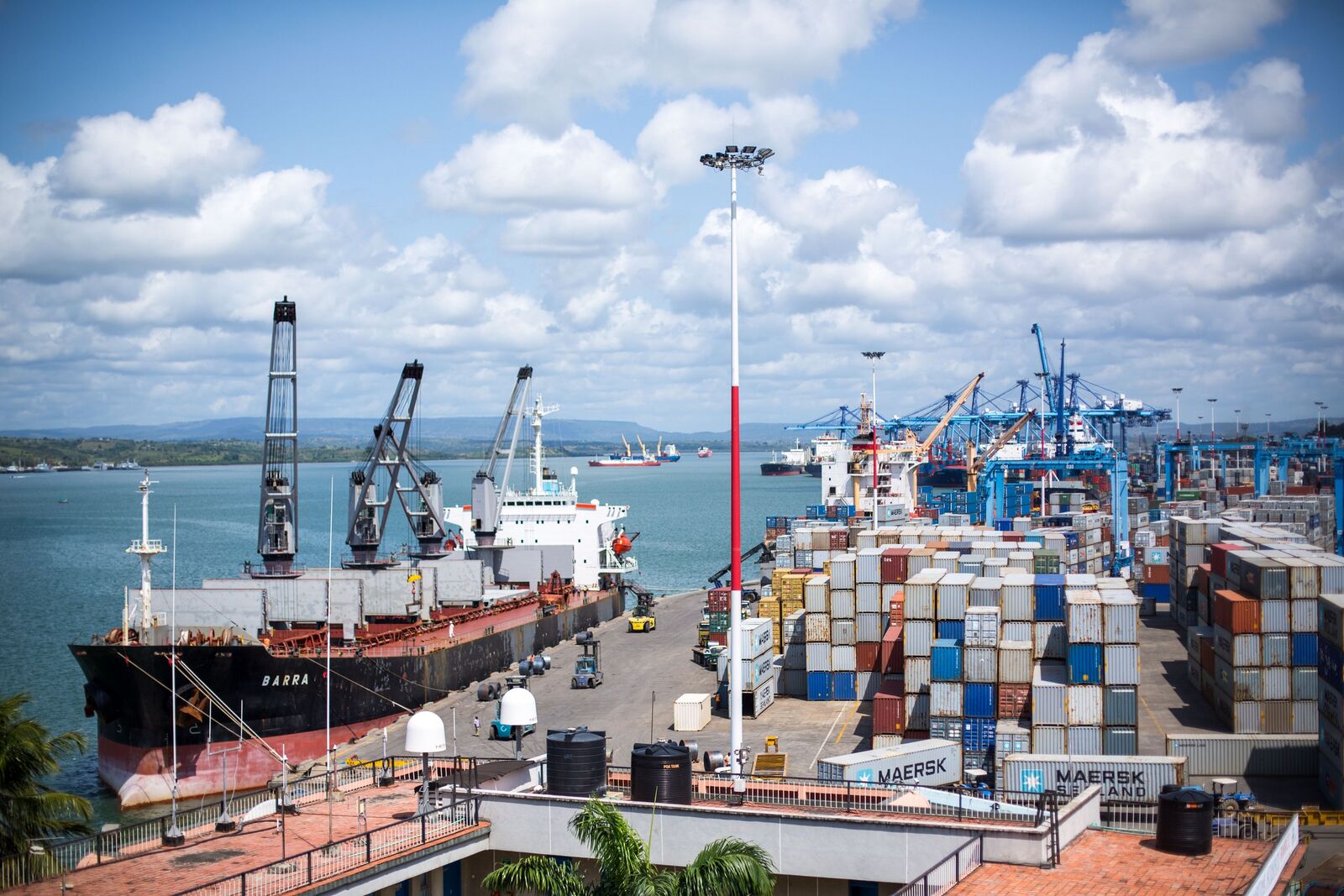 The Port of Mombasa in 2015: a bulk carrier at the quay in the foreground, stacked containers and blue container gantry cranes behind, and ships at anchor in the harbour